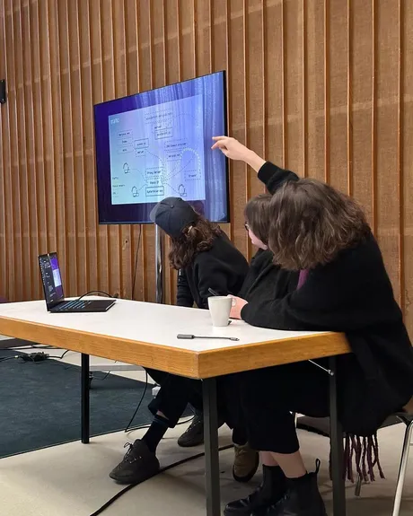 An image from a workshop In-grid did at Transmediale Content Form where members of In-gird are presenting the docs and a diagram of the network. Katie, Becky and I are sat at a table with our backs to the camera pointing to a screen behind us with the diagram of the network on it.