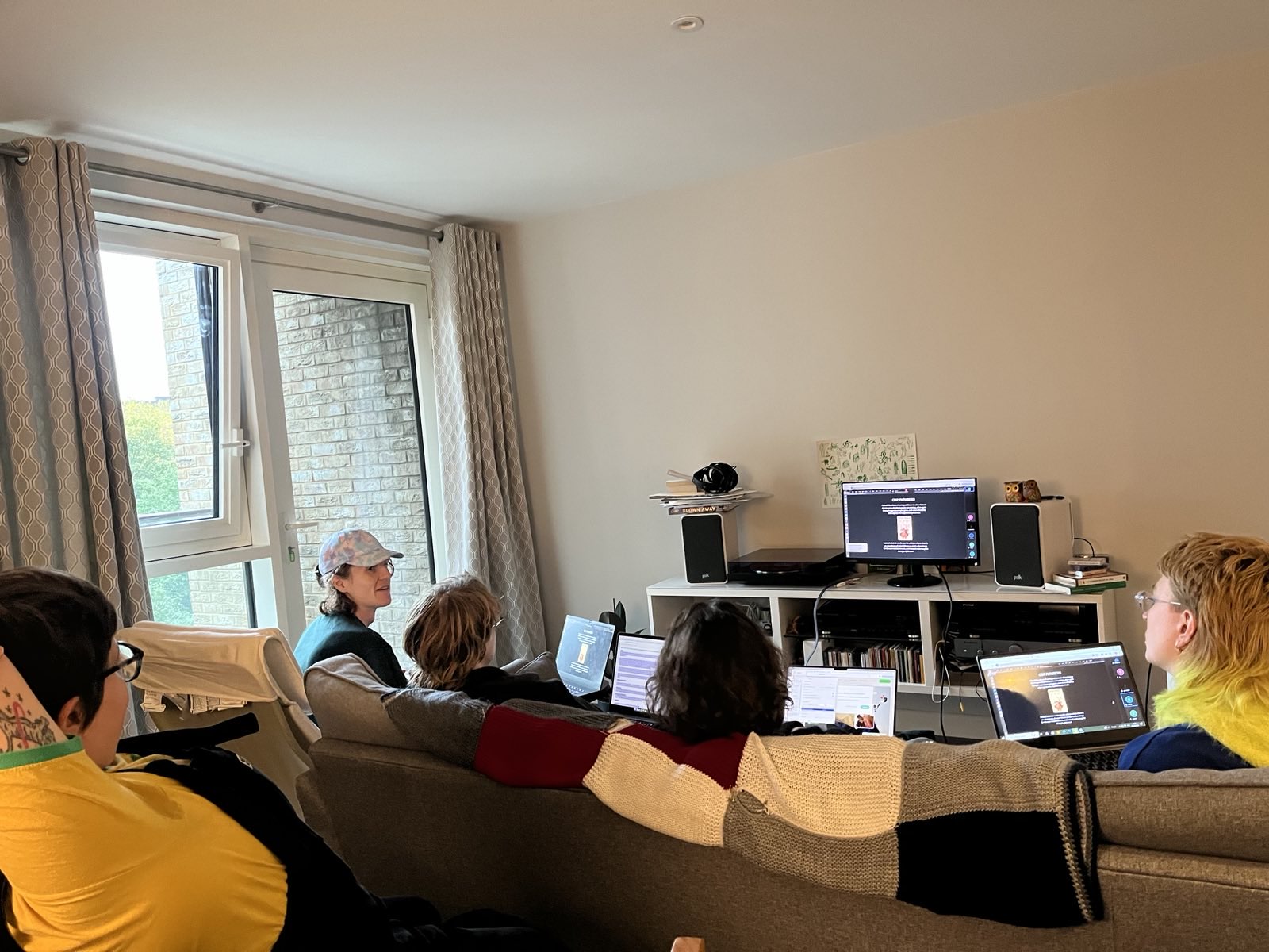 An image take from the workshop shows members of In-grid in person. We are sat comfortably on a sofa and some chairs in a kitchen/living room, with our backs to the camera.